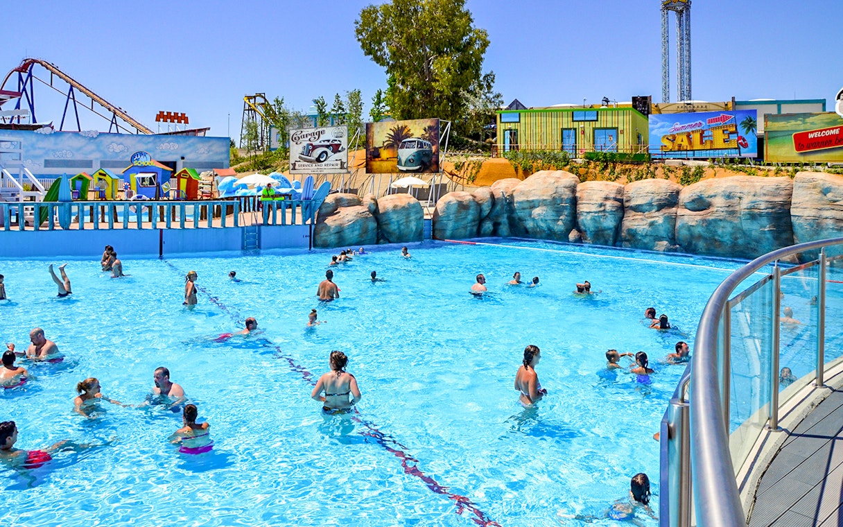 Visitors enjoying the wave pool at Parque Warner Beach, Madrid with roller coasters in the background.