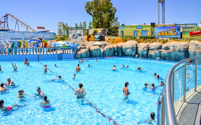 Visitors enjoying the wave pool at Parque Warner Beach, Madrid with roller coasters in the background.