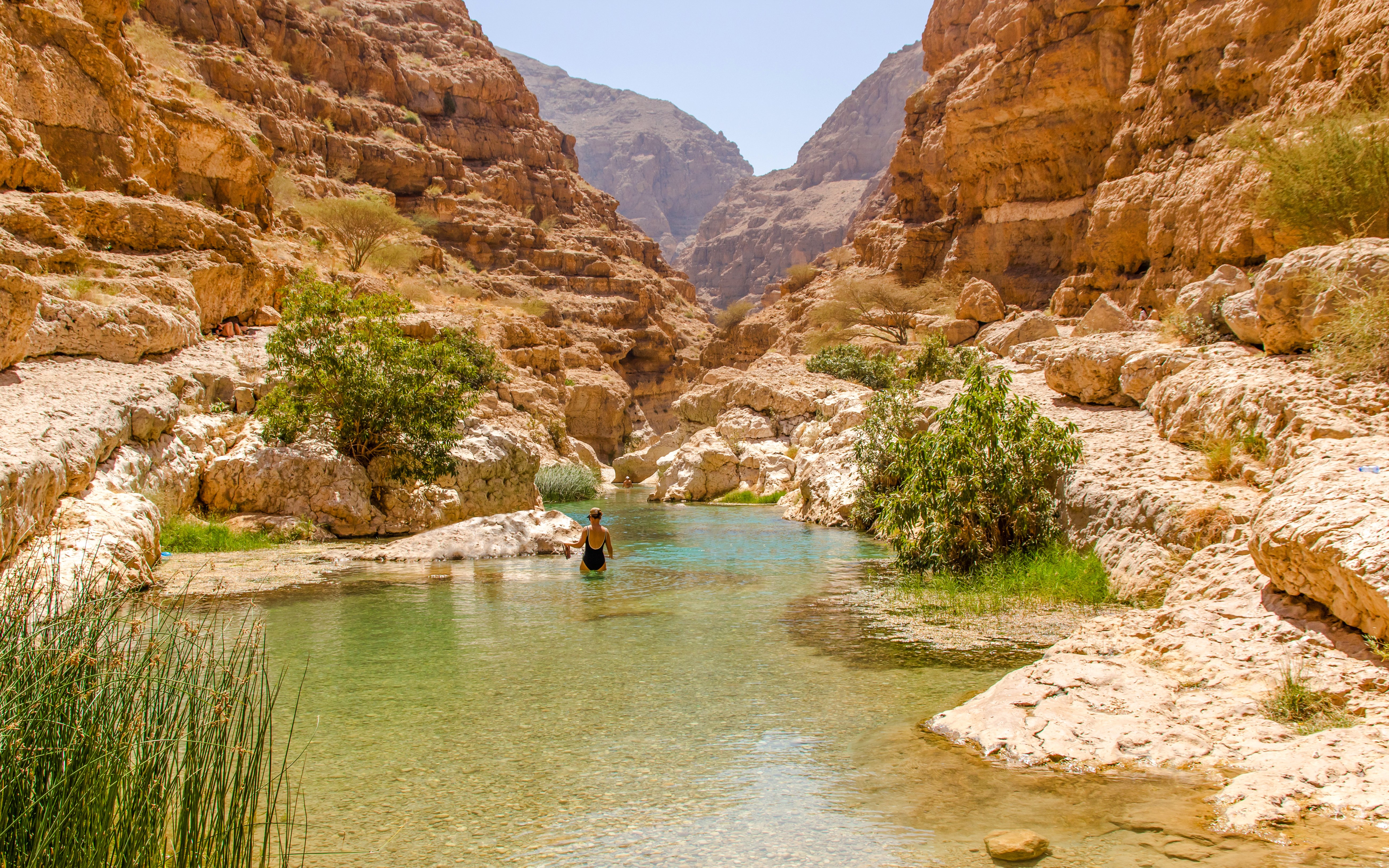 Wadi Shab in Tiwi, Oman with vertical cliffs and clear green water.