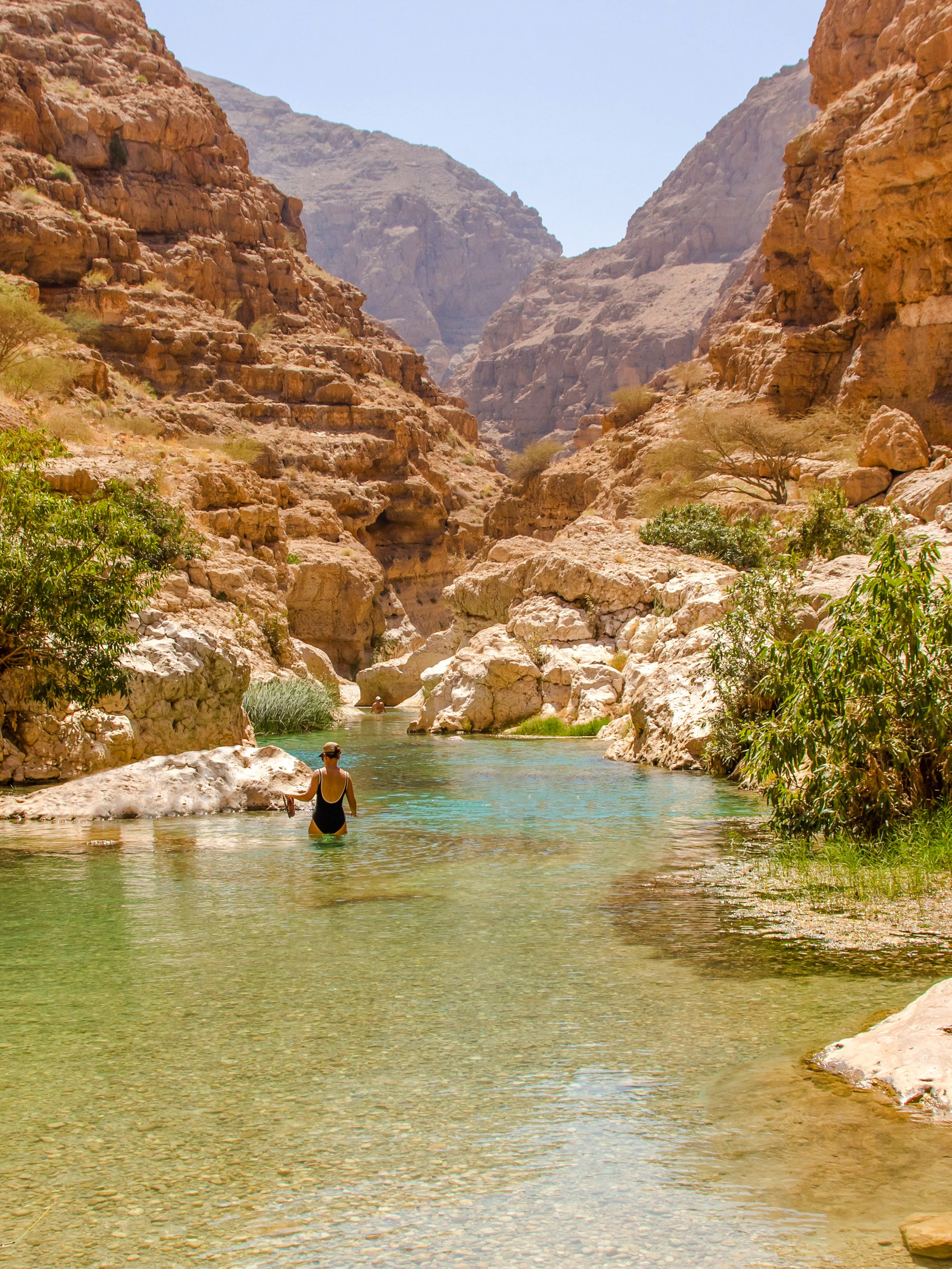 Wadi Shab in Tiwi, Oman with vertical cliffs and clear green water.