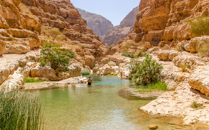 Wadi Shab in Tiwi, Oman with vertical cliffs and clear green water.