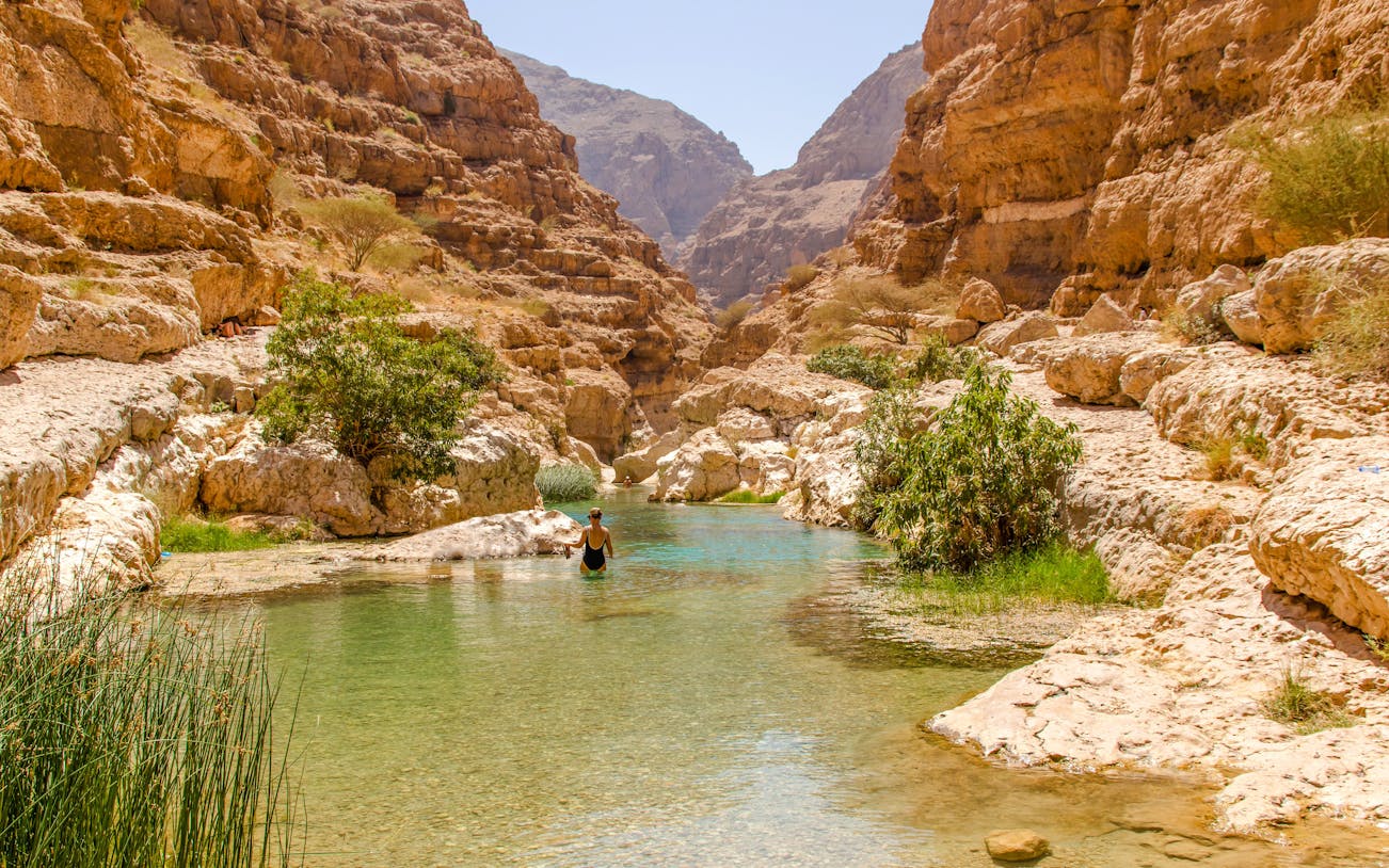 Wadi Shab in Tiwi, Oman with vertical cliffs and clear green water.