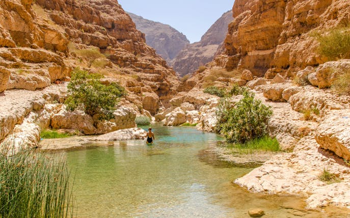 Wadi Shab in Tiwi, Oman with vertical cliffs and clear green water.