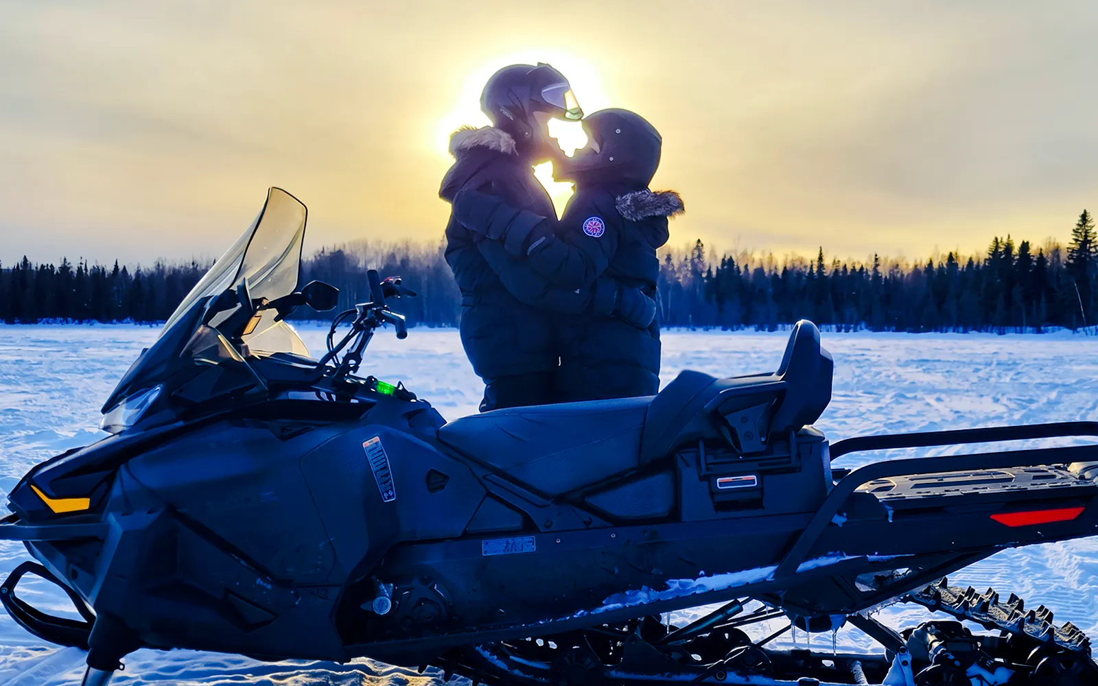 Snowmobile parked on snowy field with two people embracing, Fairbanks, Alaska.