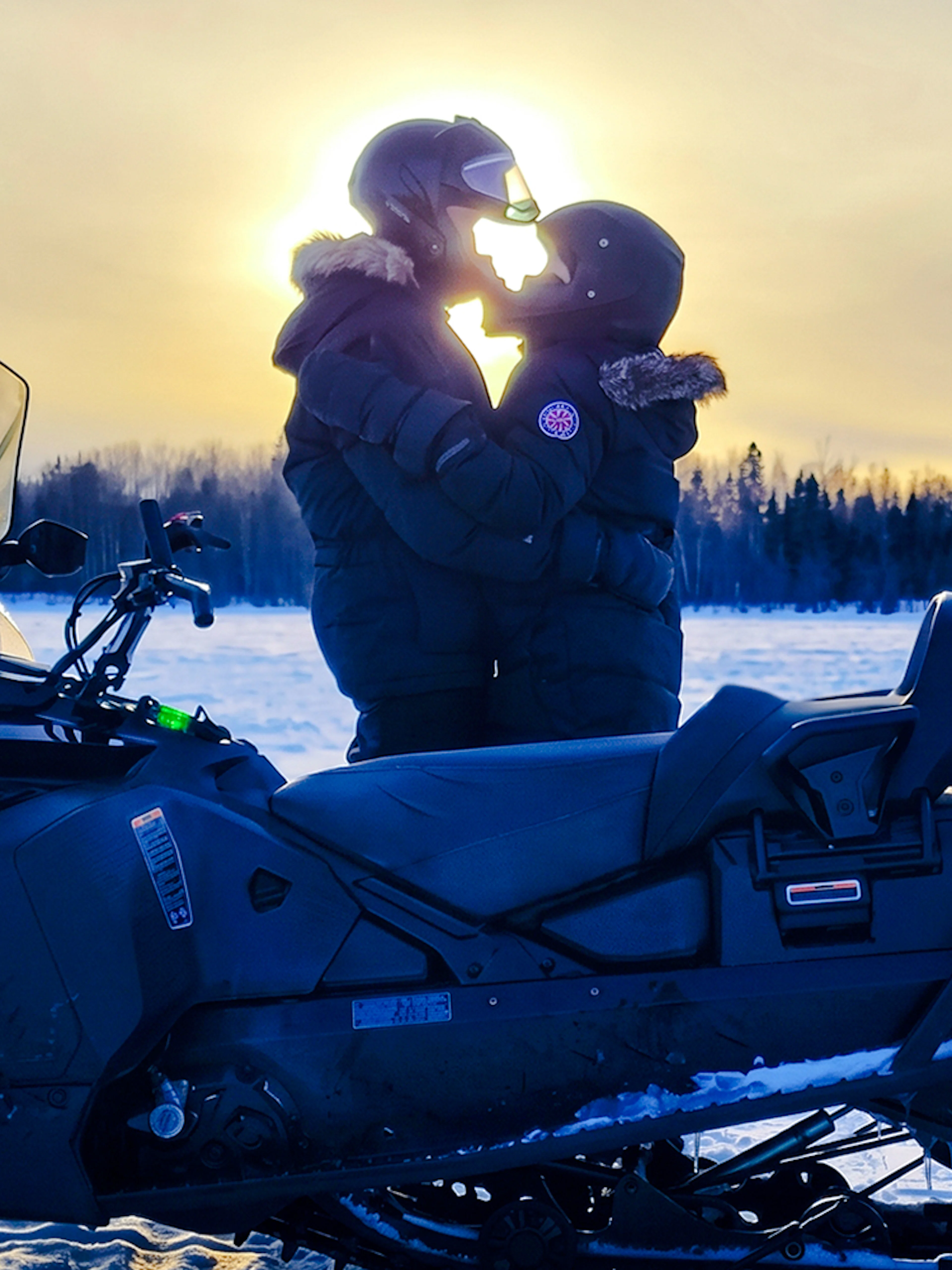 Snowmobile parked on snowy field with two people embracing, Fairbanks, Alaska.