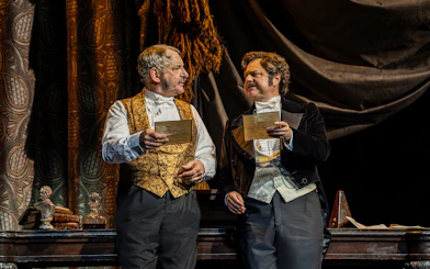 Two actors in period costumes holding letters on stage during Phantom of the Opera production.