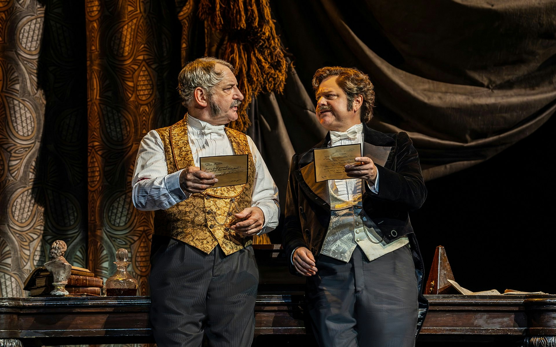 Two actors in period costumes holding letters on stage during Phantom of the Opera production.