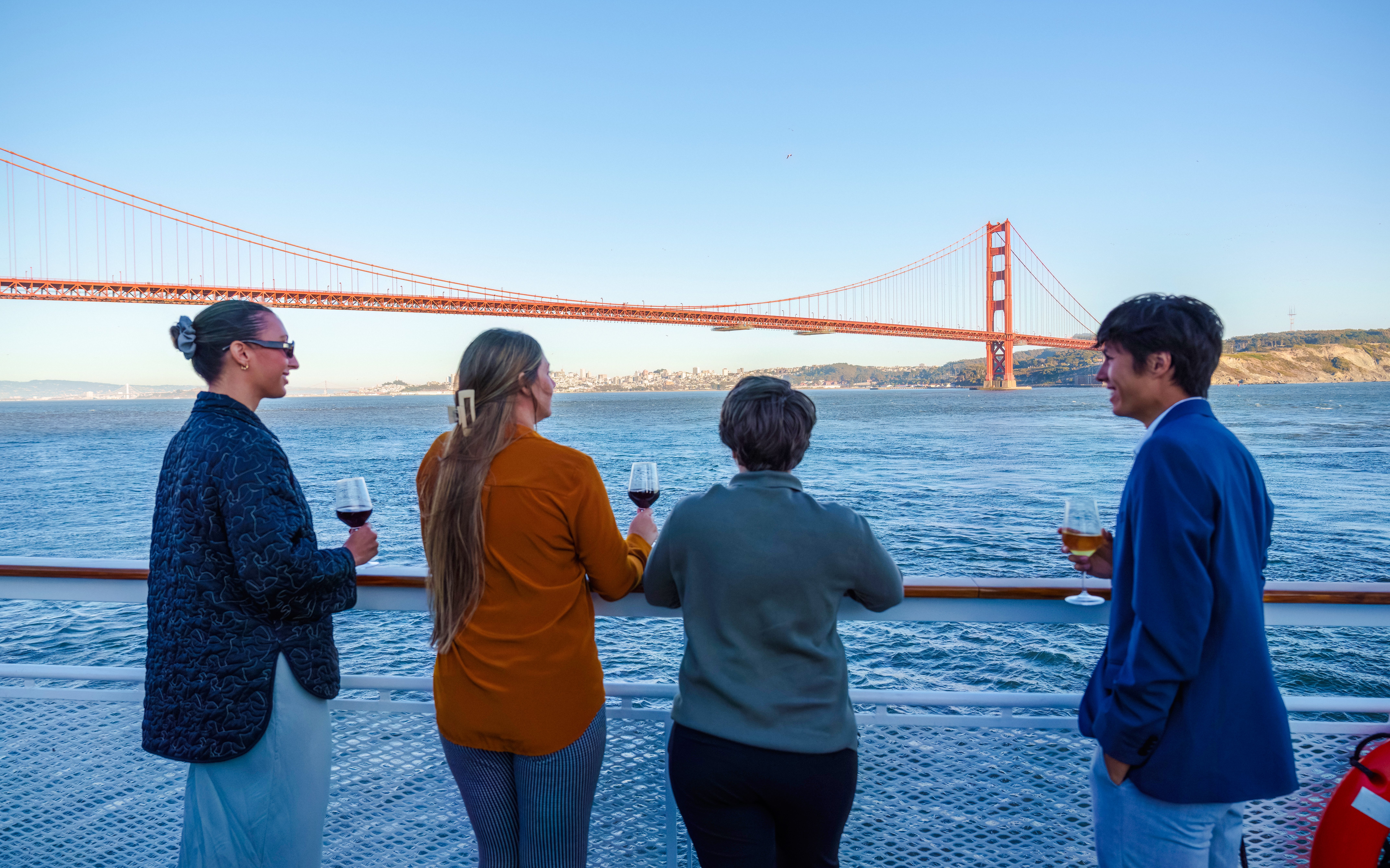 Guests enjoying drinks on a San Francisco dinner cruise with Golden Gate Bridge view.