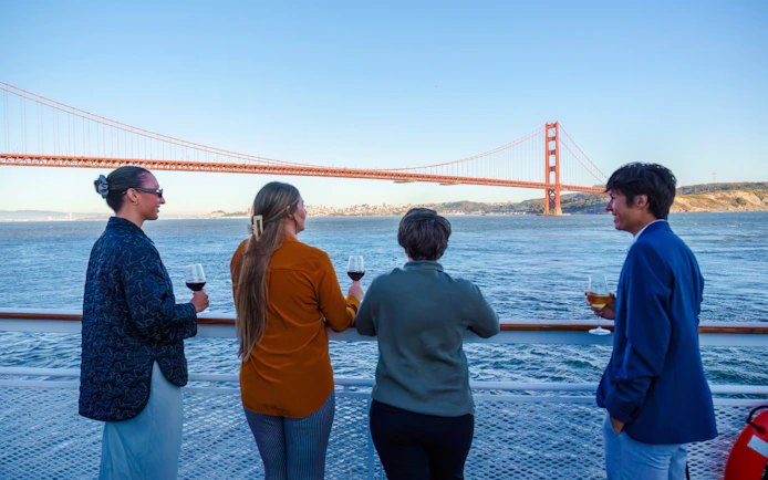 Guests enjoying drinks on a San Francisco dinner cruise with Golden Gate Bridge view.