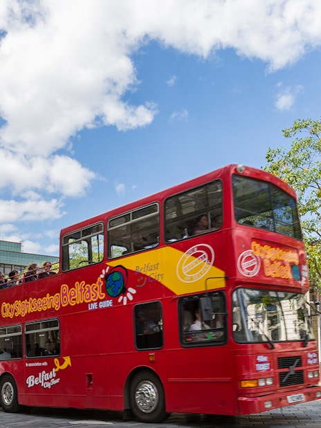 Red double-decker bus on Belfast Hop-On Hop-Off Tour passing Albert Memorial Clock.