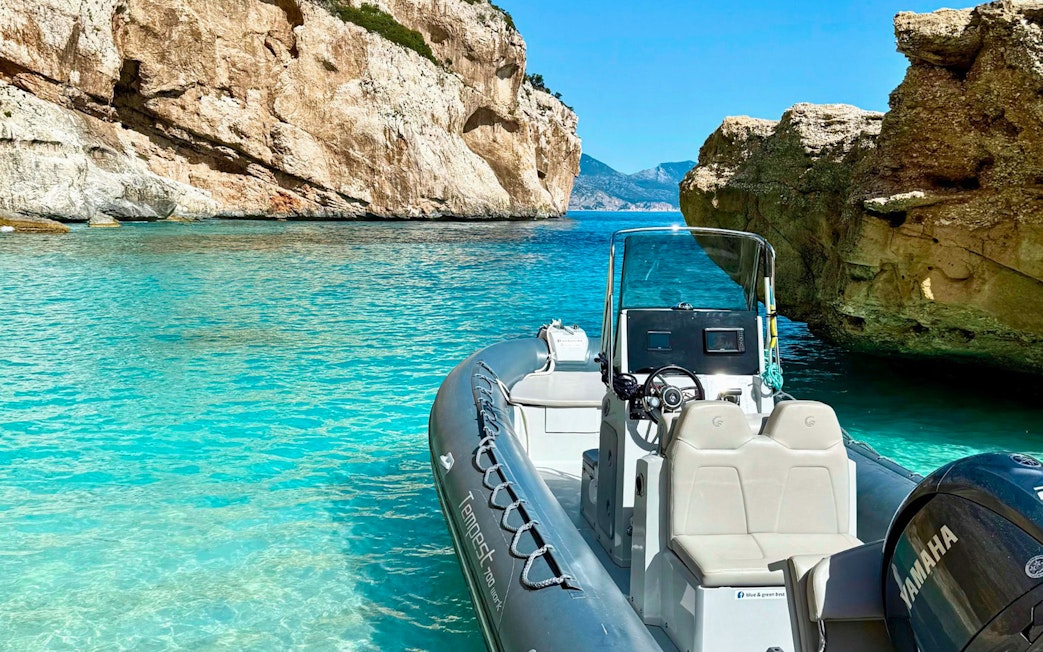 Dinghy in turquoise waters of Gulf of Orosei, Cala Gonone cliffs in background.
