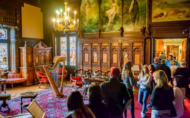 Visitors exploring the music room at Peles Castle with ornate woodwork and stained glass windows.