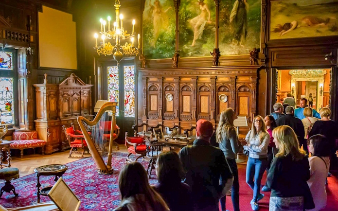 Visitors exploring the music room at Peles Castle with ornate woodwork and stained glass windows.