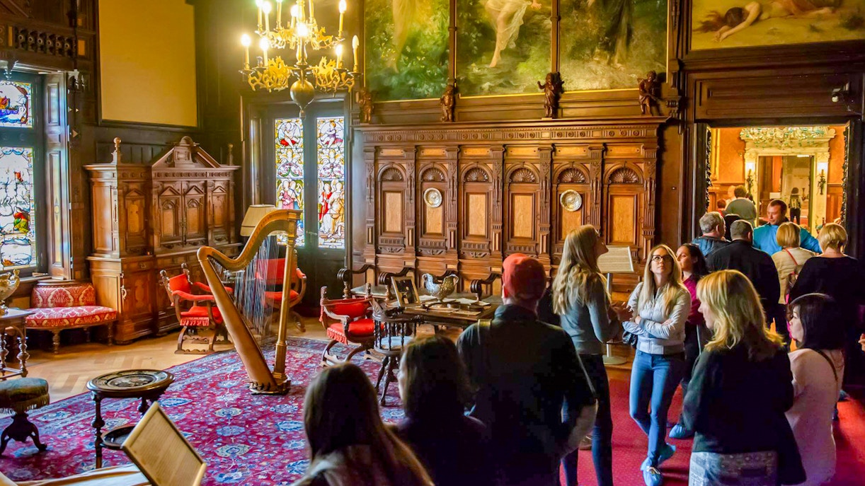 Visitors exploring the music room at Peles Castle with ornate woodwork and stained glass windows.