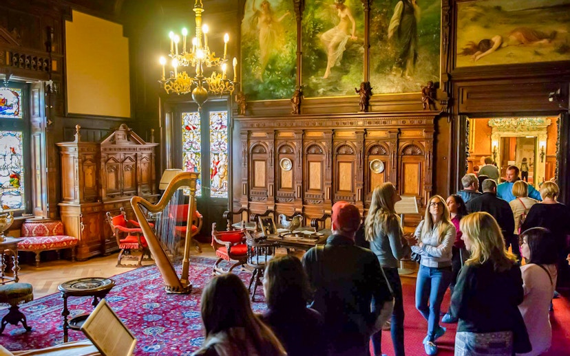 Visitors exploring the music room at Peles Castle with ornate woodwork and stained glass windows.