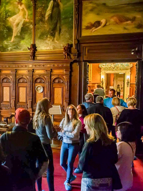 Visitors exploring the music room at Peles Castle with ornate woodwork and stained glass windows.
