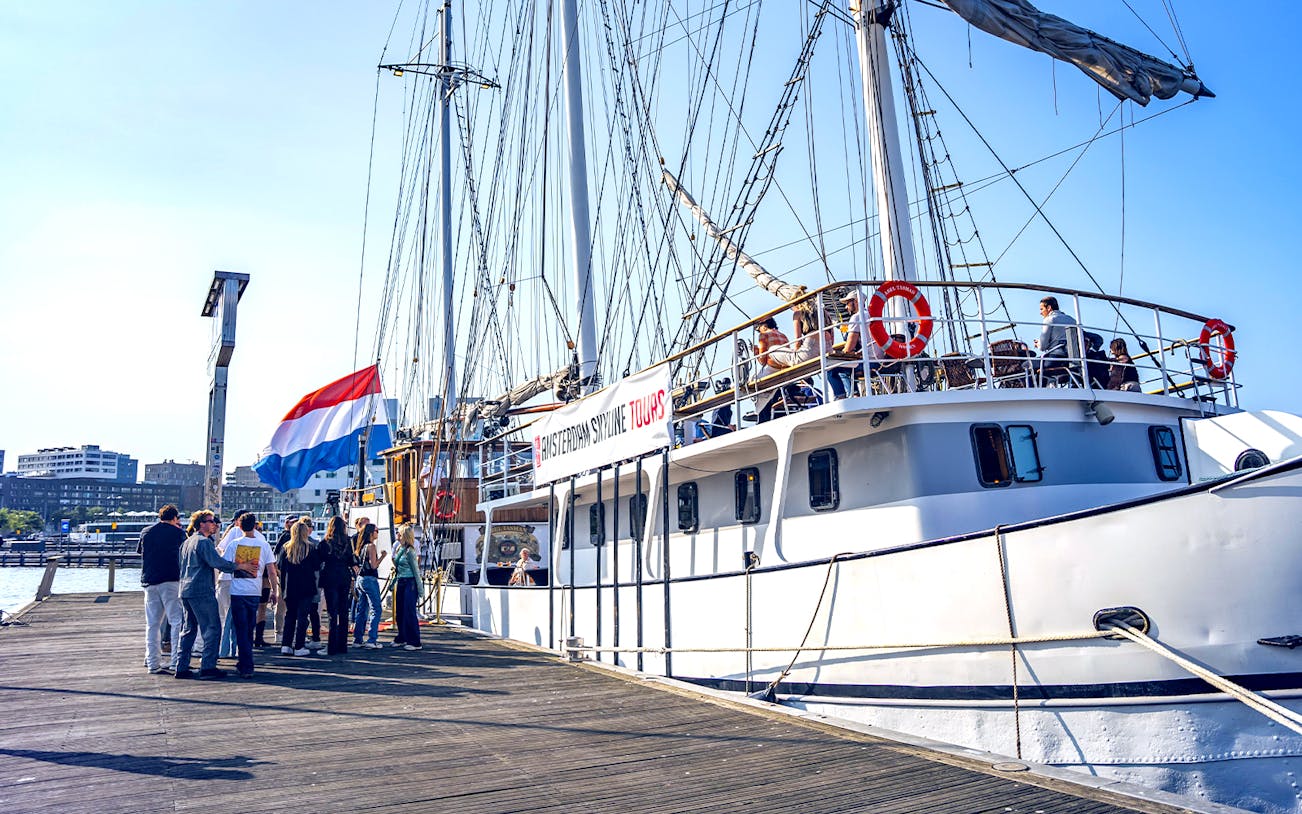 Tourists boarding a ship for Amsterdam Skyline Tours with Dutch flag visible.