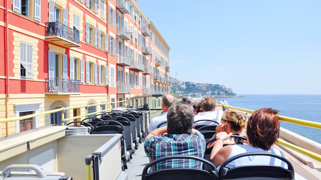 Passengers on an open-top bus tour along the French Riviera coastline.