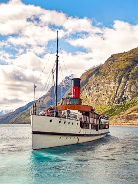 Historic steamship cruising Lake Wakatipu, New Zealand, with scenic mountain backdrop.