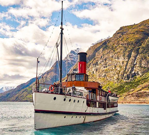 Historic steamship cruising Lake Wakatipu, New Zealand, with scenic mountain backdrop.