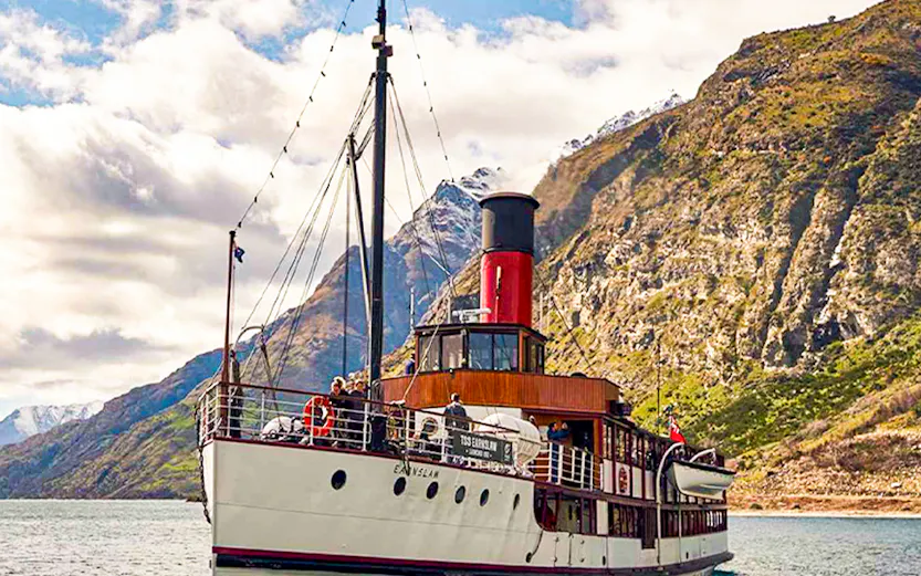 Historic steamship cruising Lake Wakatipu, New Zealand, with scenic mountain backdrop.