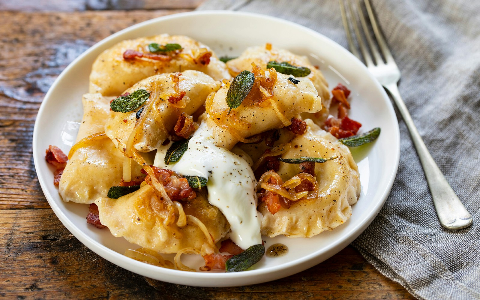 Plate of pierogi with bacon, onions, and sour cream on a wooden table.