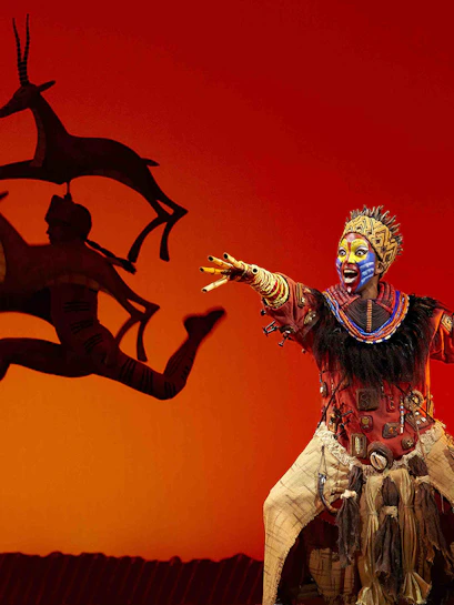 Performer in vibrant costume on stage during The Lion King show in Madrid.