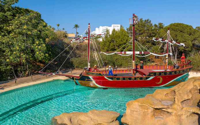 Pirate ship attraction at Terra Mitica theme park, Spain, surrounded by water and trees.