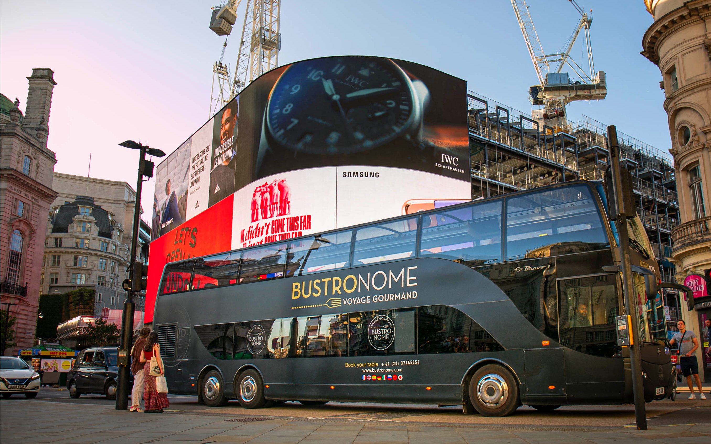Bustronome double-decker bus at Piccadilly Circus, London, with digital billboards in the background.