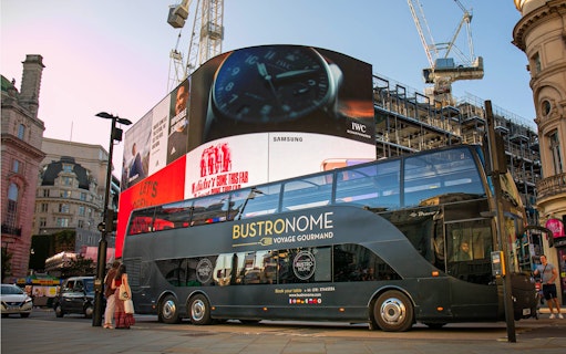 Bustronome double-decker bus at Piccadilly Circus, London, with digital billboards in the background.