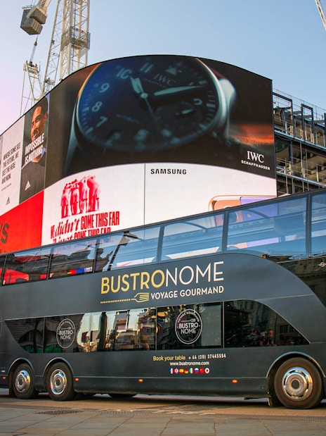 Bustronome double-decker bus at Piccadilly Circus, London, with digital billboards in the background.
