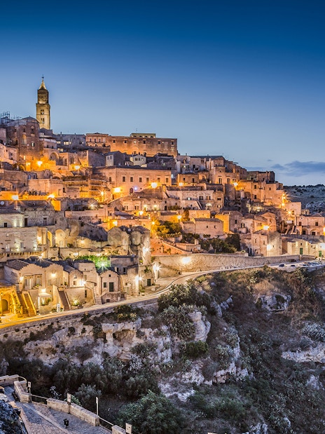 Sassi of Matera illuminated at dusk, showcasing ancient stone buildings and winding streets.