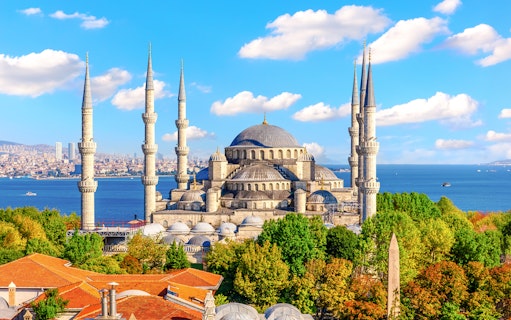 Blue Mosque exterior with minarets and domes, Istanbul skyline and Bosphorus in background.
