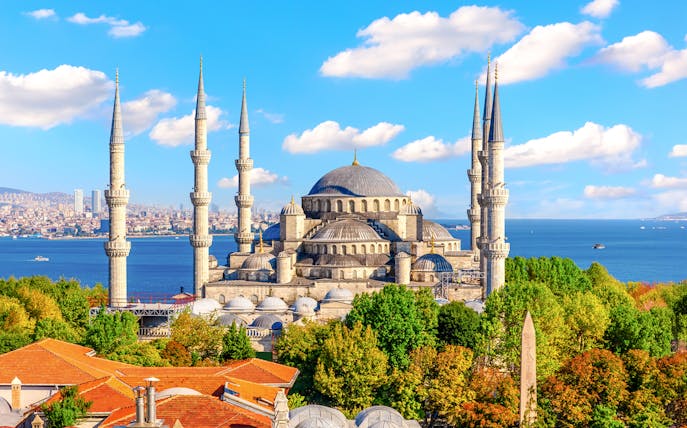 Blue Mosque exterior with minarets and domes, Istanbul skyline and Bosphorus in background.