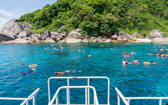 Snorkelers in clear blue water near rocky shore on Similan Islands day trip from Phuket.