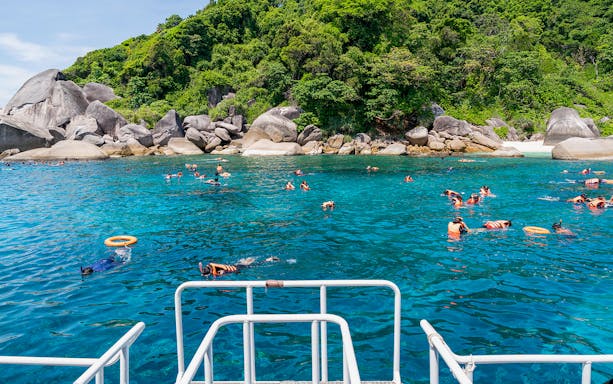 Snorkelers in clear blue water near rocky shore on Similan Islands day trip from Phuket.