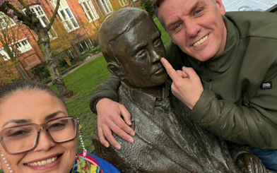 Two people posing with a statue in a Manchester park during a city exploration game.