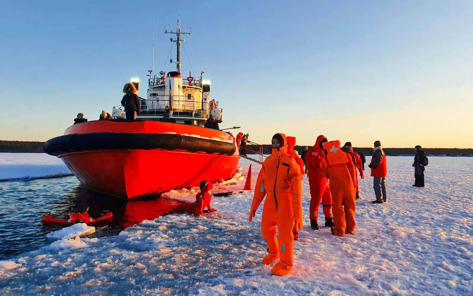 Guests in orange suits enjoying ice floating near an icebreaker ship during a cruise experience.