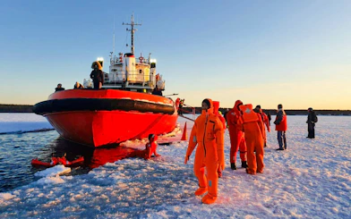 Guests in orange suits enjoying ice floating near an icebreaker ship during a cruise experience.