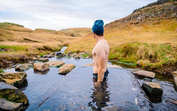 Person enjoying the warm waters of the Secret Lagoon in Iceland's scenic landscape.