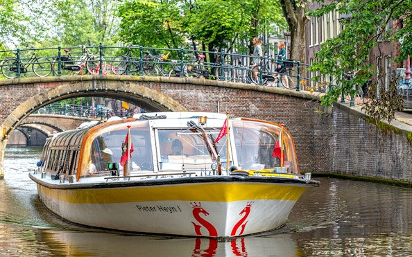Sightseeing boat on Amsterdam canal passing under a bridge with bicycles.