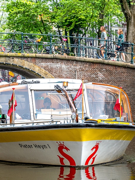 Sightseeing boat on Amsterdam canal passing under a bridge with bicycles.