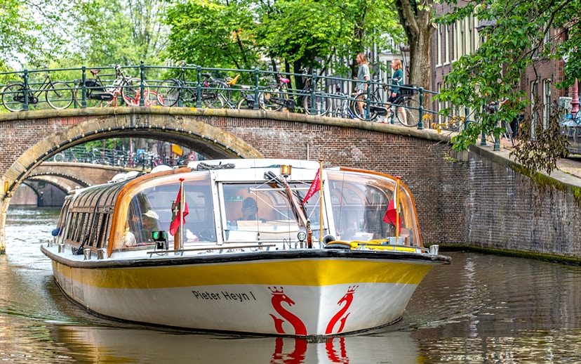Sightseeing boat on Amsterdam canal passing under a bridge with bicycles.