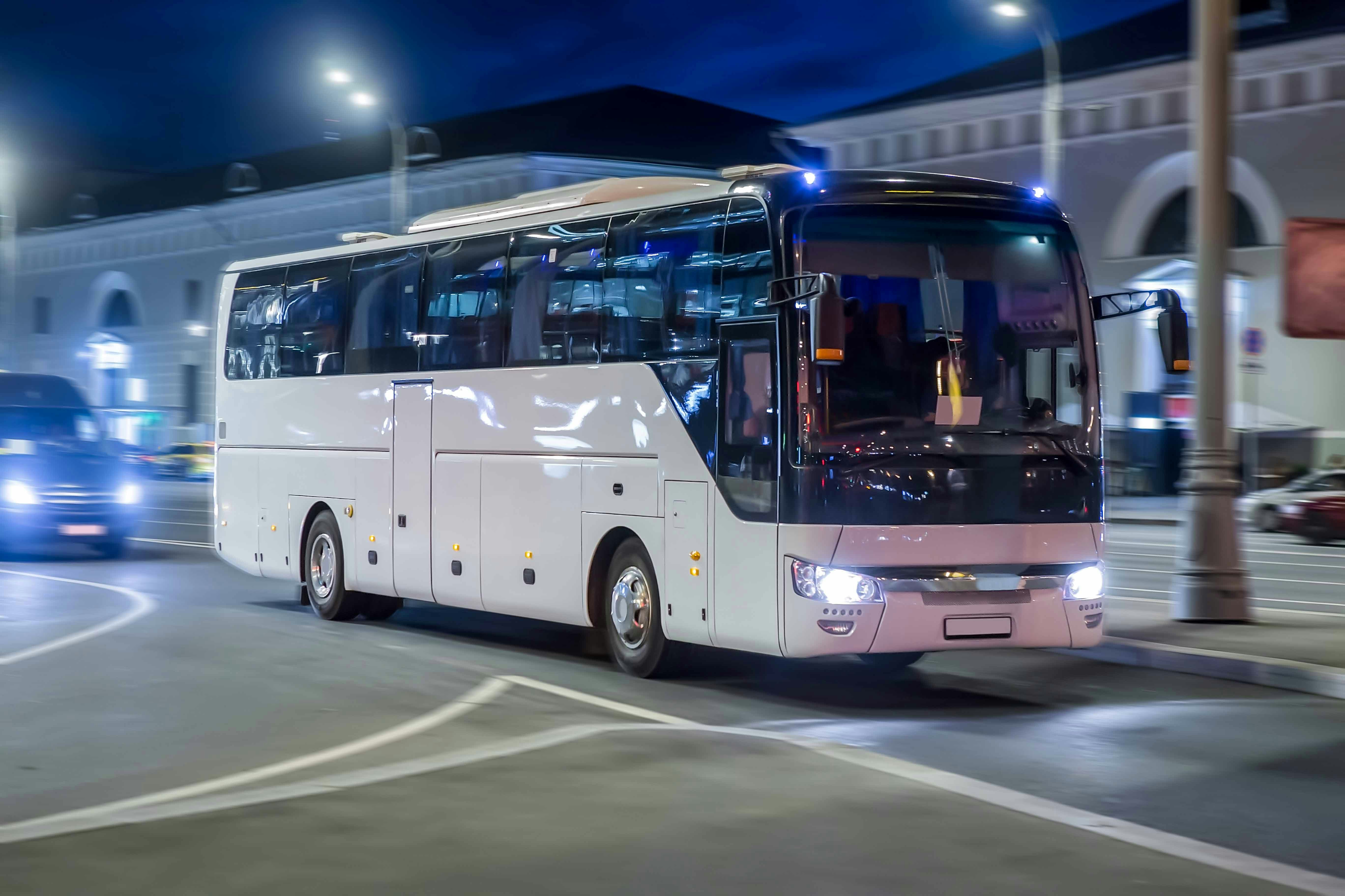 Nighttime city tour bus driving through illuminated streets.