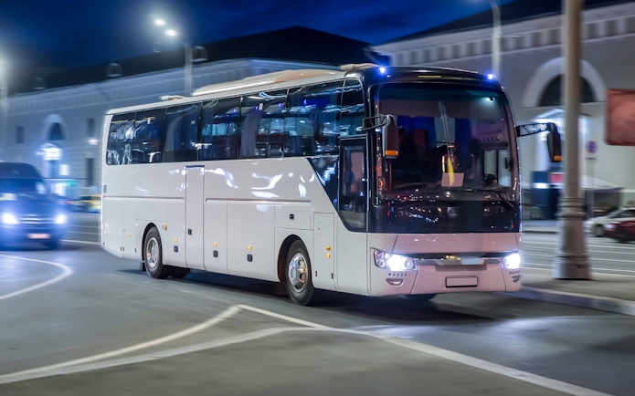 Nighttime city tour bus driving through illuminated streets.
