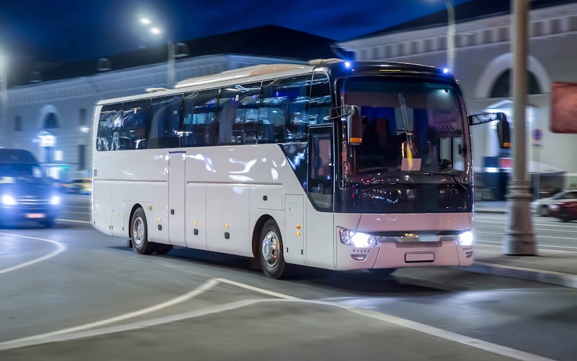 Nighttime city tour bus driving through illuminated streets.