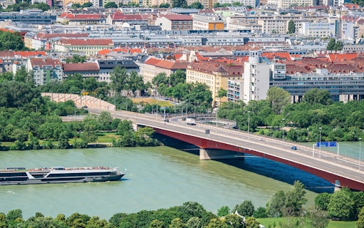 River cruise ship on the Danube with Vienna cityscape and bridge in view.