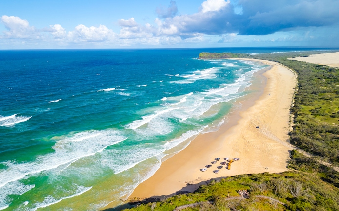 Aerial view of 75 Mile Beach on K'gari, Fraser Island, with waves and vehicles on the sand.