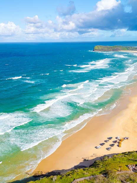 Aerial view of 75 Mile Beach on K'gari, Fraser Island, with waves and vehicles on the sand.