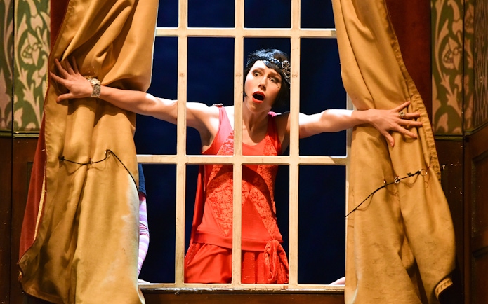 Performer in red dress on stage during "The Play That Goes Wrong" scene.